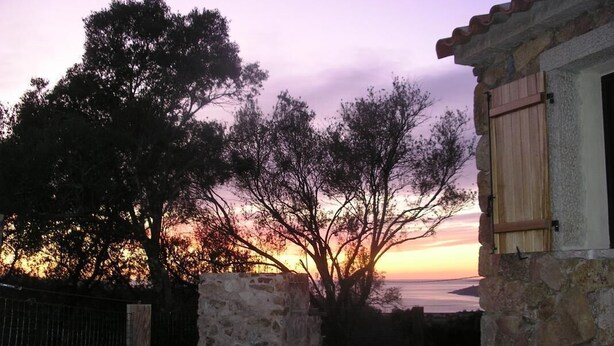 Edificio de piedra con puerta de madera y vista a árboles y un atardecer.