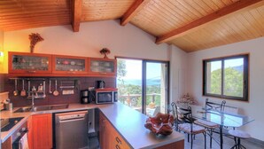 Una cocina moderna con vigas de madera, un comedor con mesa de vidrio y vistas a la vegetación.