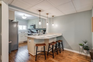 A kitchen with a central island, bar stools, pendant lights, and wooden flooring.