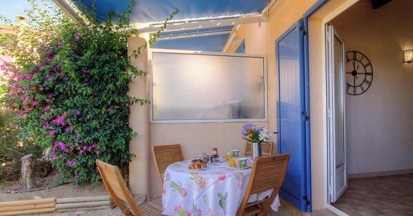 Eine Terrasse mit Tisch für zwei Personen, einer blauen Tür und einer Uhr an der Wand.