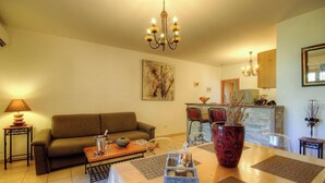 A living room with a sofa, a dining table with chairs, a chandelier, and a kitchen area in the background. - U Luminellu - LUCCIANA (LUCCIANA)