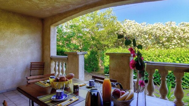 An outdoor dining area with a table set for breakfast, surrounded by greenery and a stone balustrade. - U Luminellu - LUCCIANA (LUCCIANA)