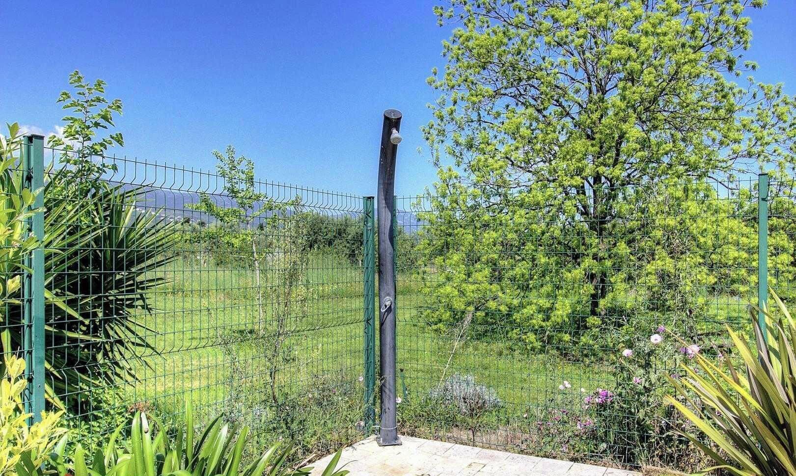 Un jardín vallado con una puerta de metal, rodeado de follaje y árboles.
