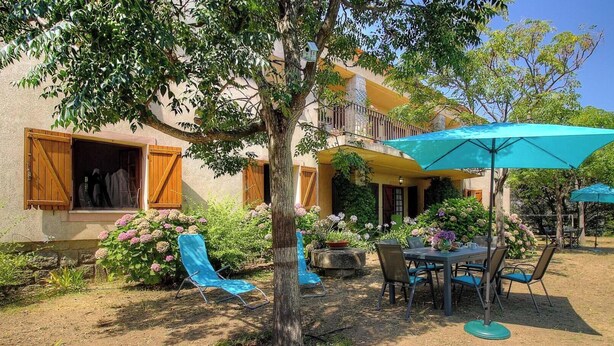 Une maison avec un balcon, un espace extérieur aménagé pour s’asseoir et un jardin.