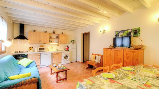Una sala de estar acogedora con sofá, una mesa de comedor preparada para dos personas y una cocina con alacenas y electrodomésticos de madera.