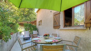 Un área de comedor al aire libre con una mesa redonda, sillas y una sombrilla verde.