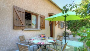 Un patio con una mesa lista para dos personas, rodeado de sillas y una sombrilla que da sombra.