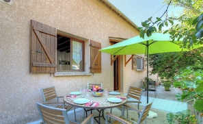 Eine Terrasse mit Tisch für zwei Personen, umgeben von Stühlen und einem Sonnenschirm.