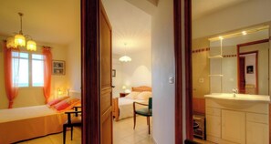 Ein Hotelzimmer mit Bett, Sessel, Schreibtisch, Lampe, Spiegel und einem Badezimmer mit Waschbecken und Toilette.
