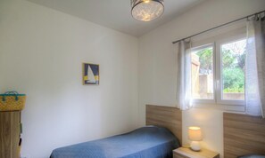 Ein Schlafzimmer mit einem Einzelbett, einem Nachttisch mit Lampe, einem Fenster mit Vorhängen und einem Wandbild.