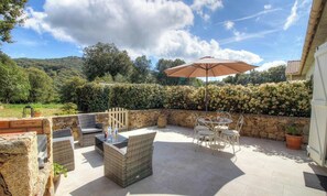 Eine Terrasse im Freien mit Korbmöbeln, einer Steinmauer und Blick auf die Landschaft.