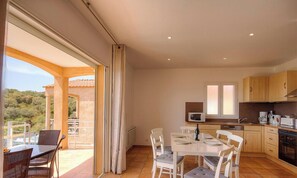 Eine moderne Küche mit weißen Schränken, einer Mikrowelle und einem Herd. Es gibt einen Essbereich mit Tisch und Stühlen sowie einen Balkon mit Blick auf die Landschaft.