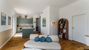 A modern interior with a sofa, a marble table, a wooden floor, a kitchen area, and a bookshelf. - L'Écrin Lumineux avec double balcon - Welkeys (Arcachon)