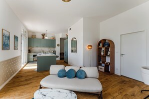 Ein modernes Interieur mit einer Couch, einem Marmortisch, Holzboden, einer Küchenzeile und einem Bücherregal.