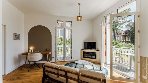 A modern living room with a sofa, a TV, a fireplace, and a large sliding glass door to a balcony. - L'Écrin Lumineux avec double balcon - Welkeys (Arcachon)