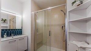 A modern bathroom with a glass shower enclosure, a white vanity with a mirror, and a shelf with toiletries. - L'Écrin Lumineux avec double balcon - Welkeys (Arcachon)