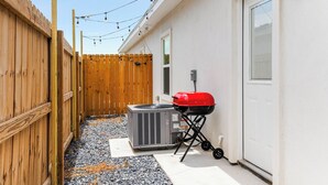 A backyard with a wooden fence, an air conditioning unit, a barbecue grill, and string lights. - The Cozy Ridge Apartment (Edinburg)