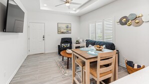 A modern living space with a dining area, a sofa, a ceiling fan, and a flat-screen TV mounted on the wall. - The Cozy Ridge Apartment (Edinburg)