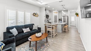 A modern kitchen with white cabinets, a central island, and a dining area with a wooden table and chairs. - The Cozy Ridge Apartment (Edinburg)