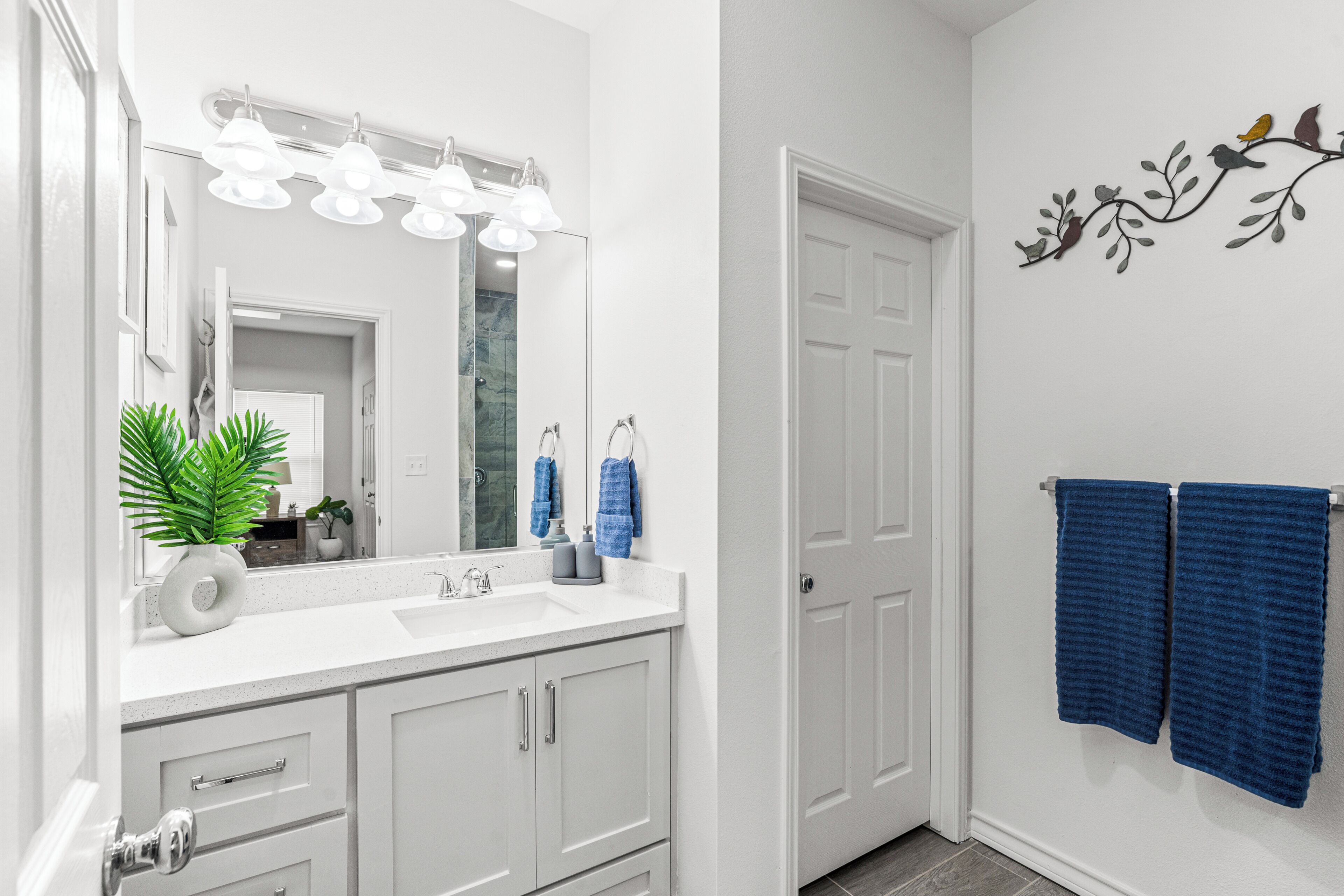 A bathroom with a white vanity, a mirror, a sink, and a towel rack with blue towels.