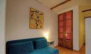 A room with a teal sofa, a wooden door with red curtains, and a wall-mounted abstract painting. - Petirossu - CAGNANO - Guest house (CAGNANO)