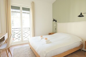 A bedroom with a bed, a desk, a chair, a bedside table, a lamp, and a view through a window. - Appartement avec Rooftop à Montpellier - Welkeys (Montpellier)