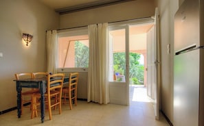 A room with a dining table and chairs, a door leading to an outdoor area, and a wall-mounted light fixture. - 10673 - SAINTE LUCIE DE PORTO VECCHIO (SAINTE LUCIE DE PORTO VECCHIO)