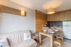 A compact kitchen with wooden cabinets, a dining table with chairs, and a bench. - Le Cocon du Gollet - Welkeys (Megève)