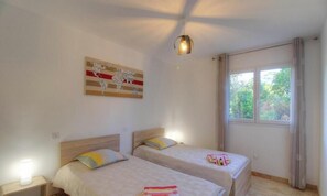 Ein Schlafzimmer mit zwei Betten, einem fensterbelaubten Fenster, einer Wandleuchte und einem Wandbild mit einer Landkarte.