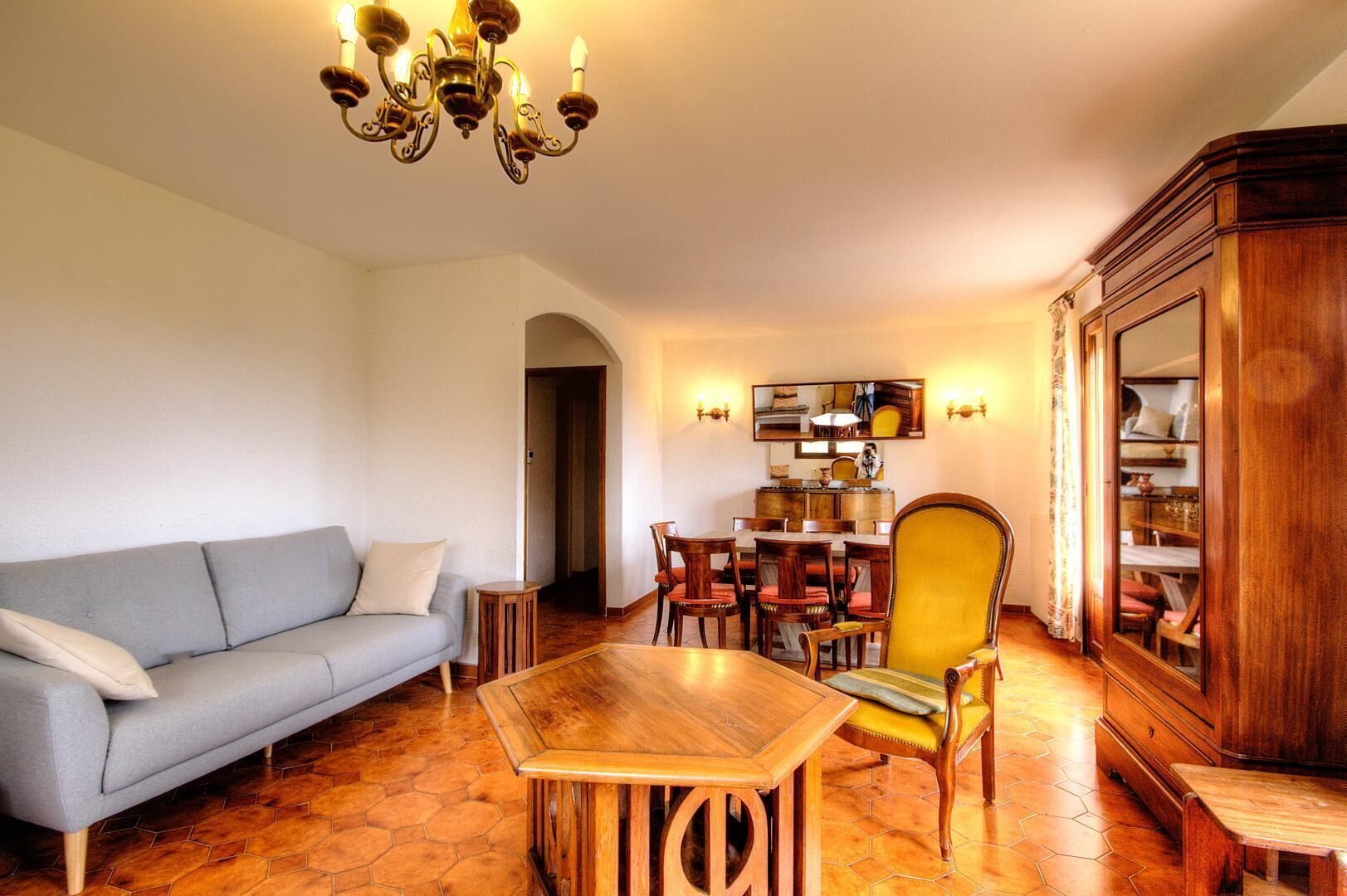 Una sala de estar con sofá, mesa de centro de madera, sillón amarillo, mesa de comedor con sillas y un aparador de madera.