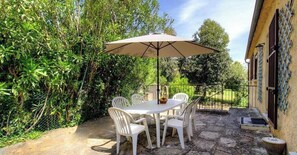 Een terras buiten, met een tafel en stoelen, omringd door groen.