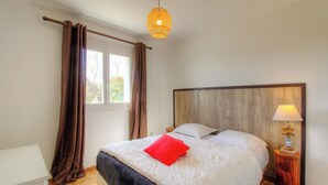 Ein Schlafzimmer mit Bett, Vorhängen, einem Fenster, einer Nachttischlampe und einem hölzernen Kopfteil.