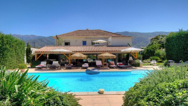 Una casa con piscina, poltrone da esterno e ombrelloni.