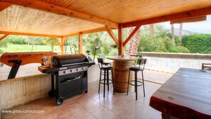 Una terrazza esterna con una griglia per barbecue, un tavolo rotondo in legno e sgabelli da bar.