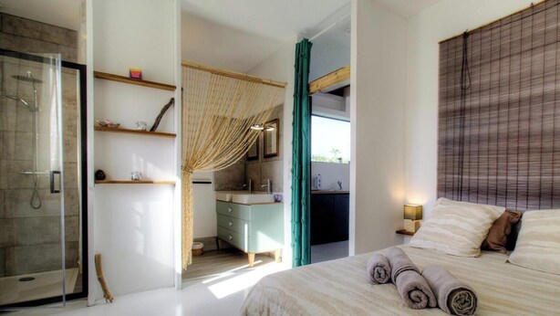 Une chambre à coucher comprenant un lit, une table de chevet, une commode, une salle de bain avec une douche, un lavabo et un miroir.