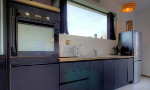 Eine moderne Küche mit Einbauofen, Mikrowelle und Kühlschrank, einem Fenster mit Vorhängen und einer Pendelleuchte.