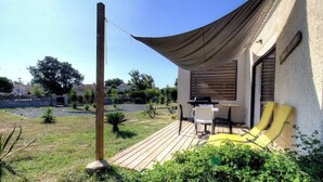 Une terrasse avec une table et des chaises, un barbecue et deux fauteuils de jardin jaunes.