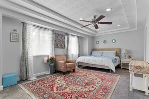 Ein Schlafzimmer mit einem Bett, einem Sessel, einem Teppich, einem Deckenventilator und einem Nachttisch mit einer Lampe.