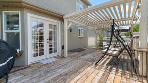 Un patio couvert doté d’une terrasse en bois, d’une pergola et d’une porte-fenêtre coulissante donnant sur un espace extérieur.