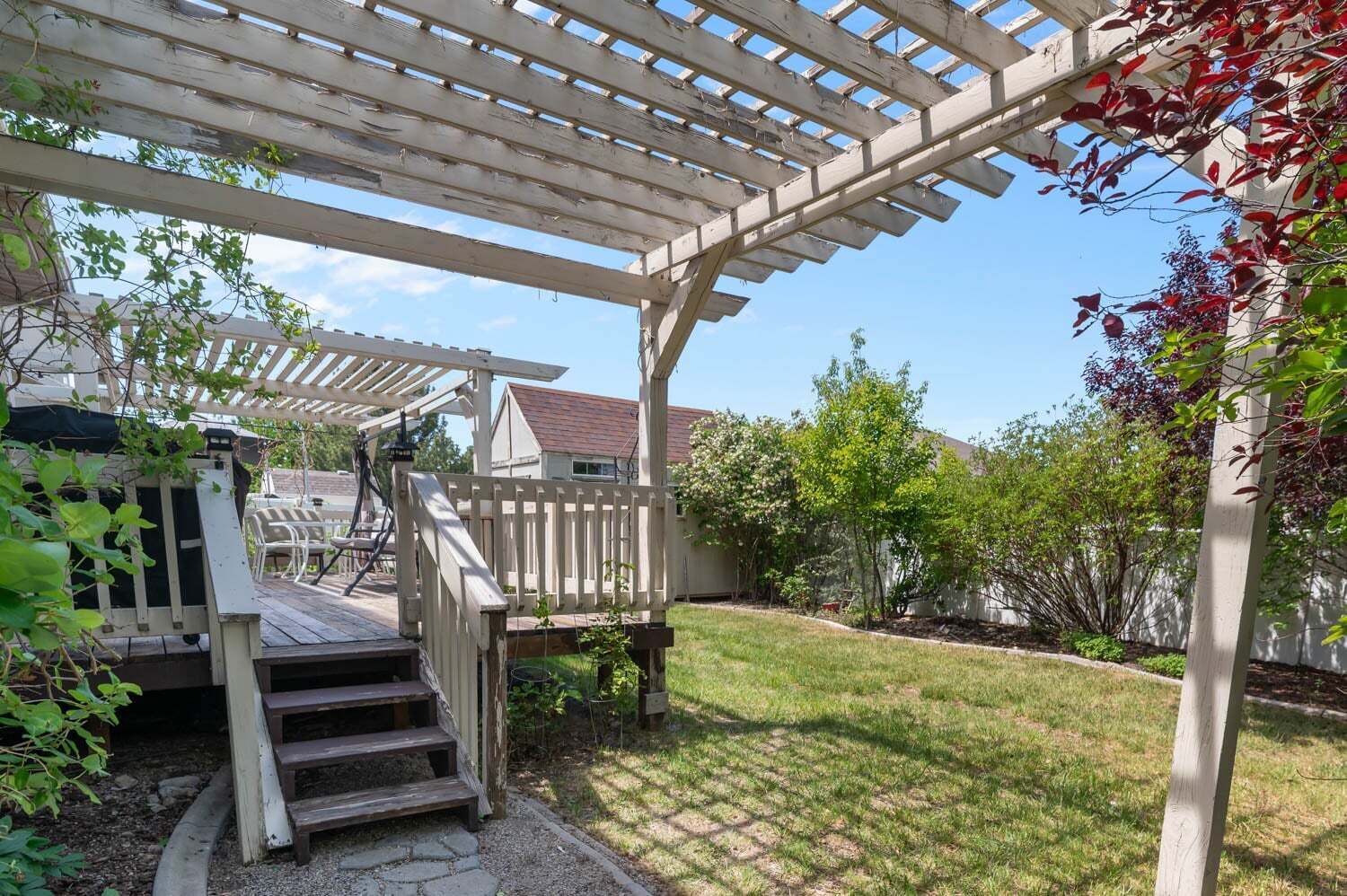 En træterrasse med pergola, en lille trappe og en patio med udendørs møbler.