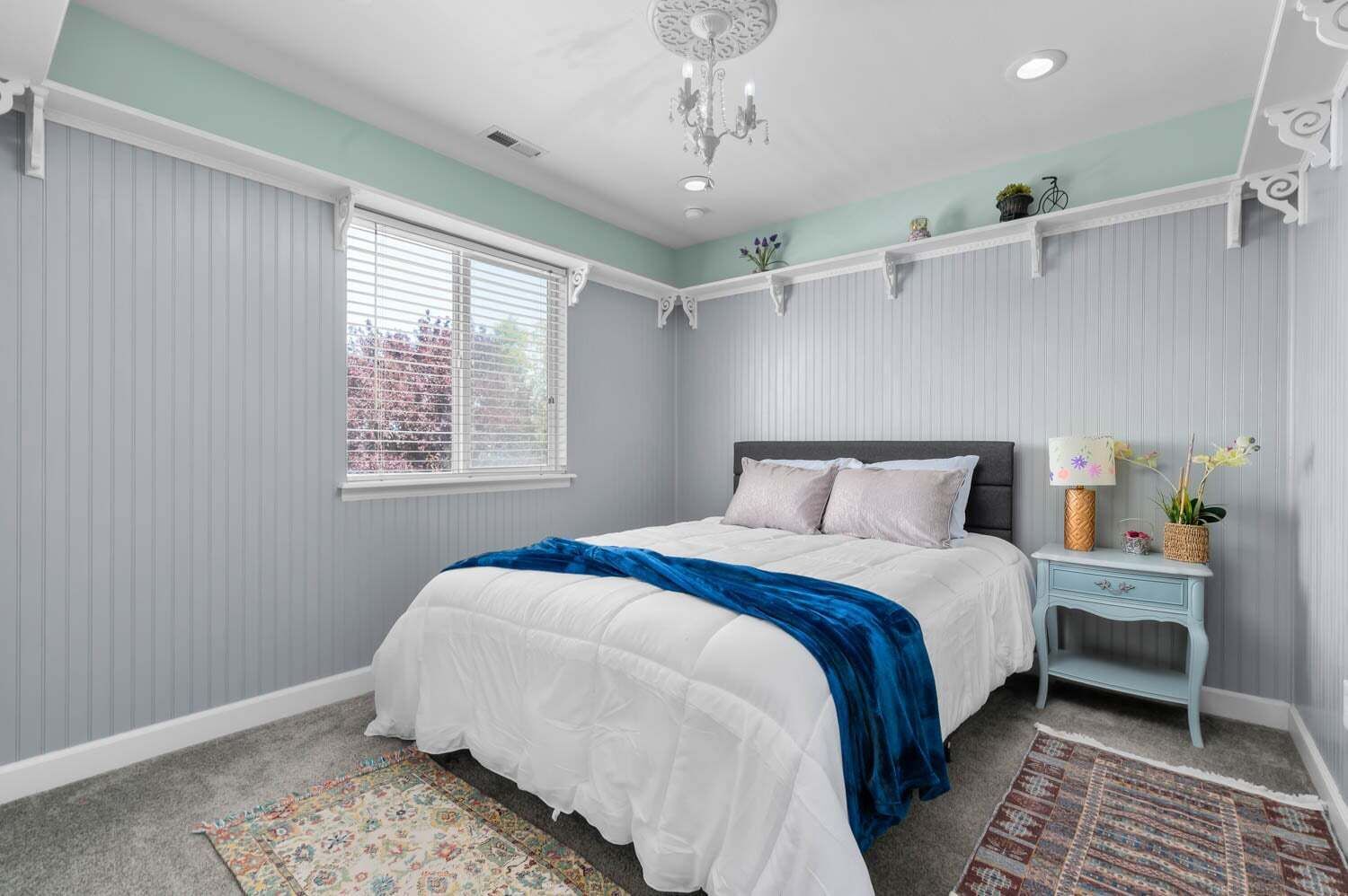 A bedroom with a bed, a nightstand, a lamp, and a window with blinds.