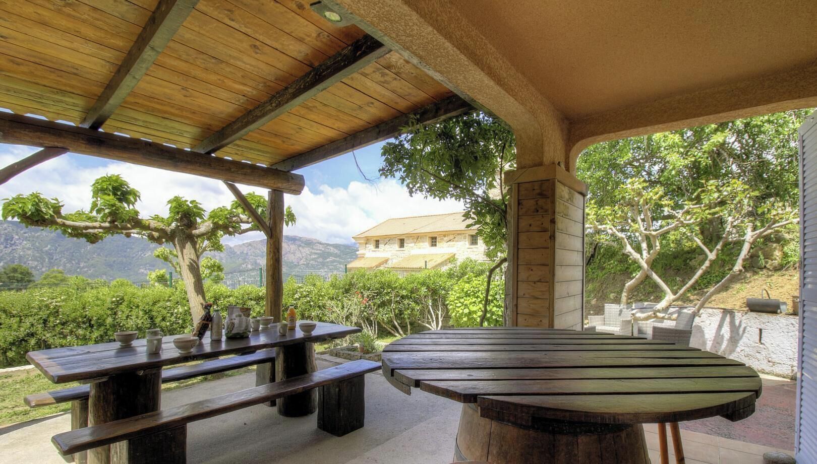 A covered outdoor seating area with wooden tables and benches, overlooking a mountainous landscape.