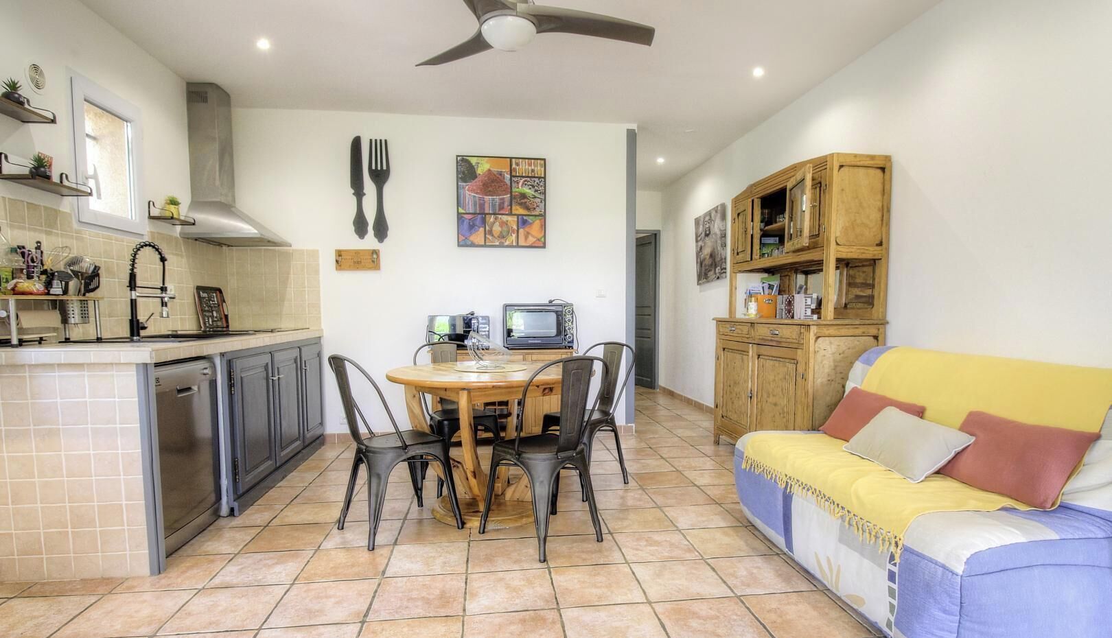 A compact kitchen with a dining area, a ceiling fan, and a sofa with cushions.