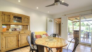 Een kamer met een houten kast, een ronde tafel met stoelen, een plafondventilator en een schuifdeur van glas die uitkomt op een buitengebied.