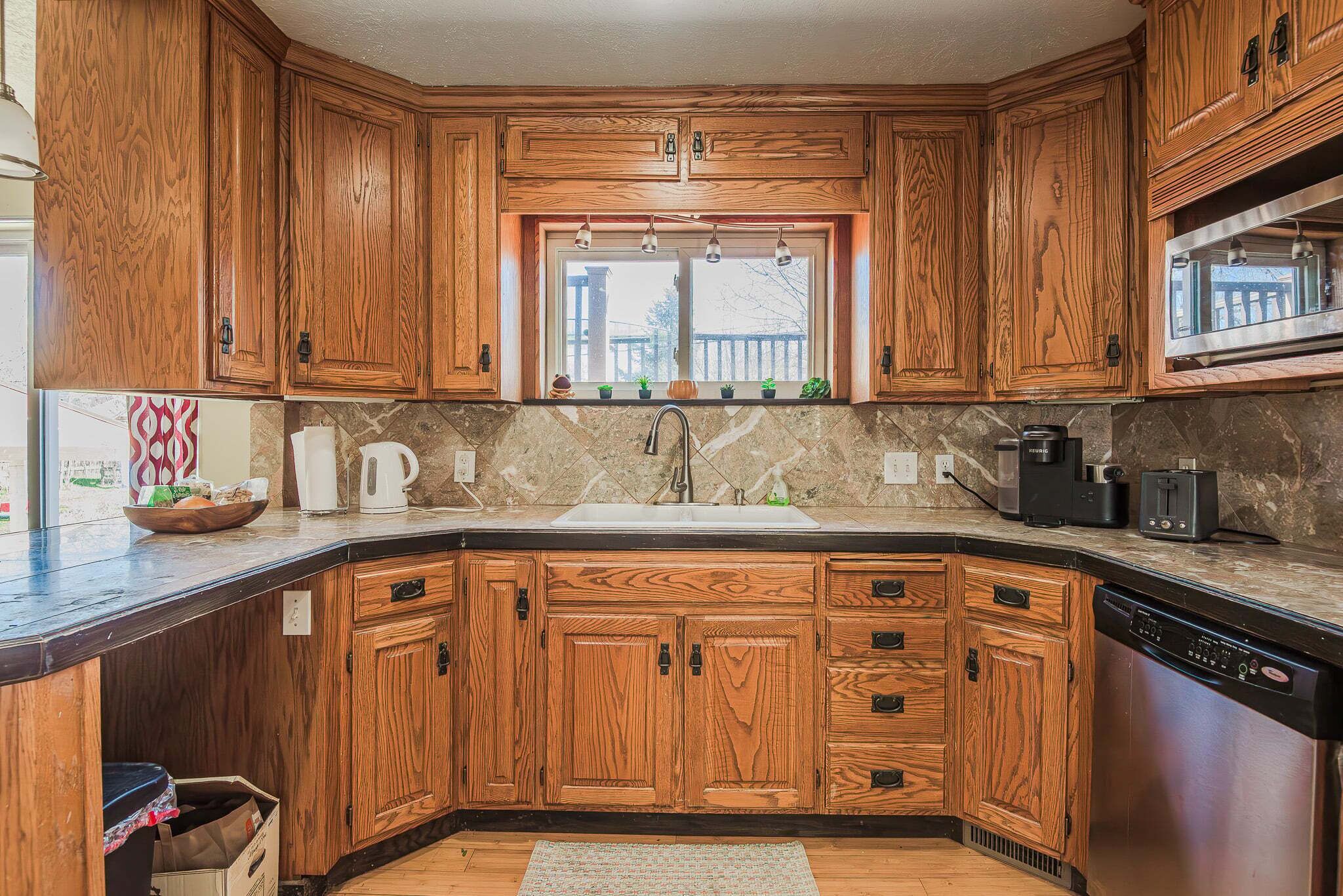 A kitchen with wooden cabinets, a sink, a window, and a dishwasher.