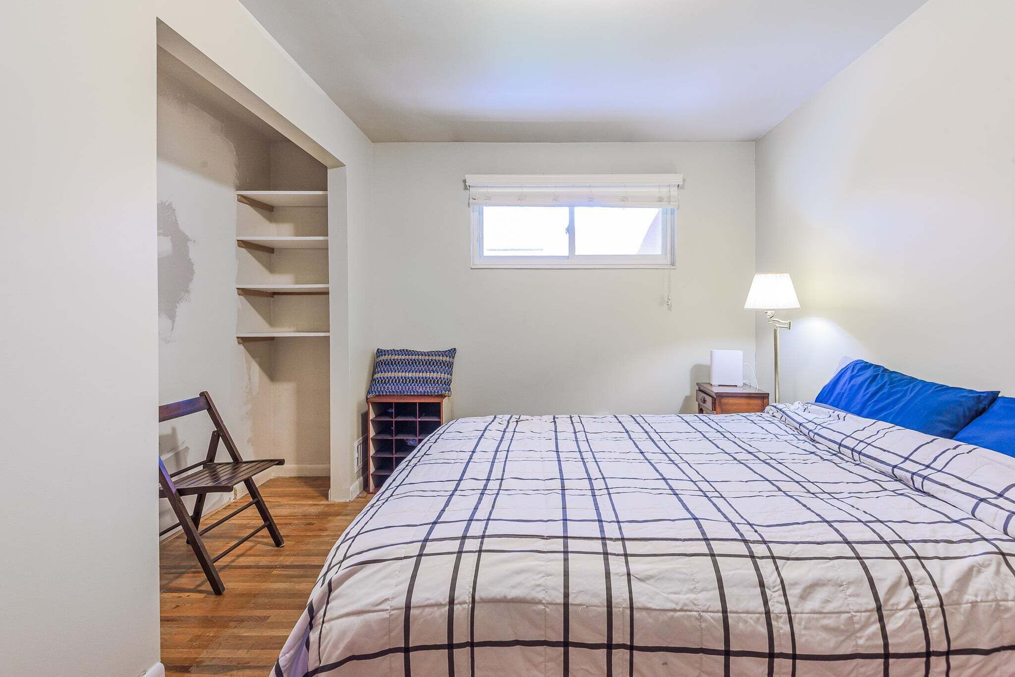 Ein Schlafzimmer mit Bett, Fenster, Stuhl, Lampe und Regalelement.