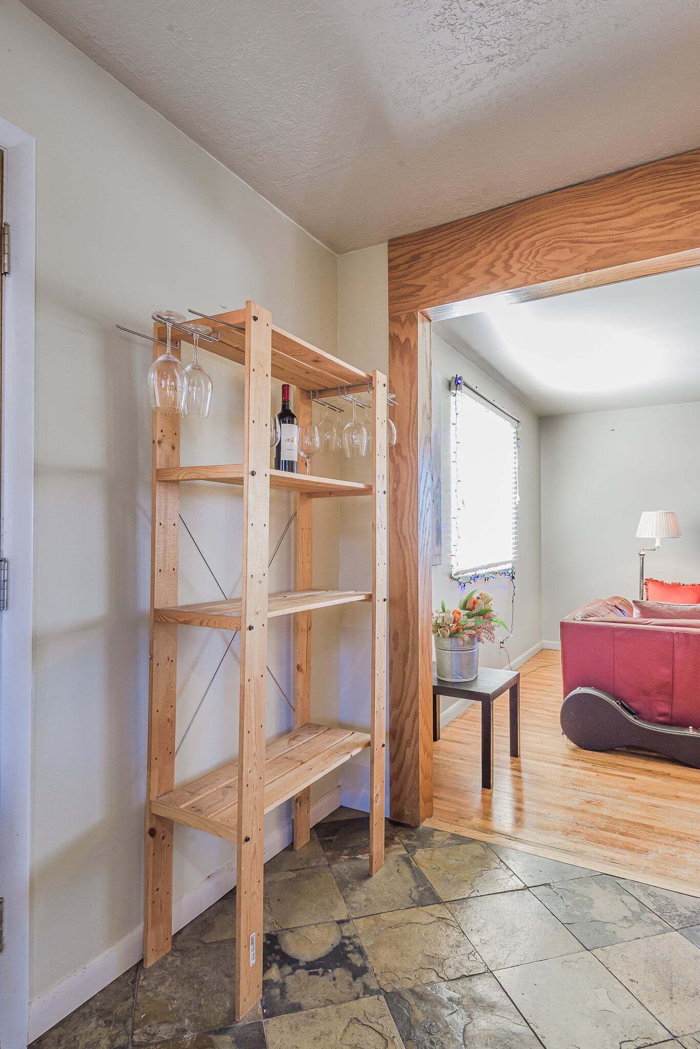 Una habitación con una estantería de madera, un sofá rojo, una mesita con un florero y una ventana con persianas.