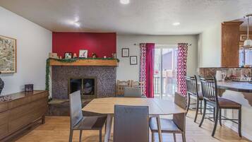 A dining area with a fireplace, wooden furniture, and a view to the outside.