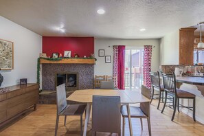 A dining area with a fireplace, wooden furniture, and a view to the outside.