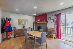 Un coin repas avec une table et des chaises en bois, une cheminée et une vue à travers une porte-fenêtre coulissante.